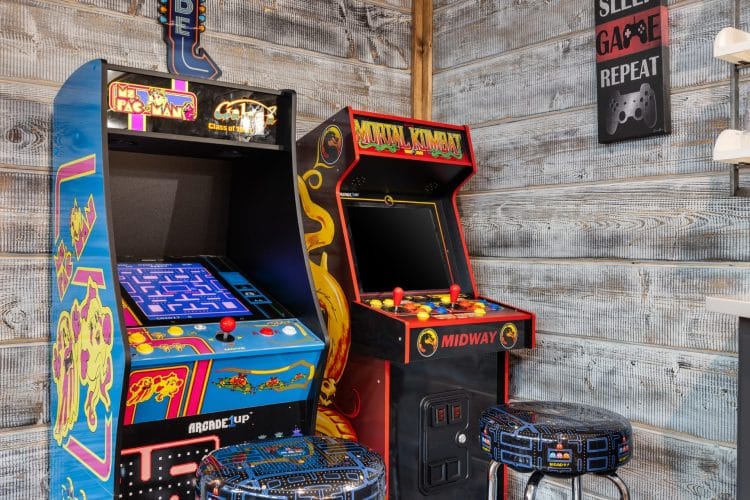 Two arcade cabinets with stools beside a wall sign