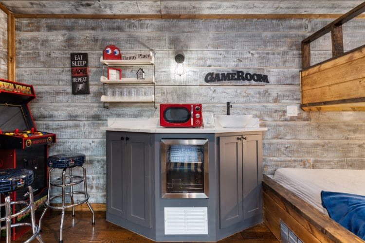 Kitchenette with gray cabinets, a mini fridge and a red microwave, with a bunk bed beyond
