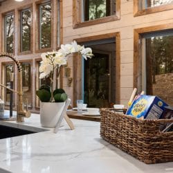Kitchen sink and counter in front of tall windows, with a basket of cereal boxes