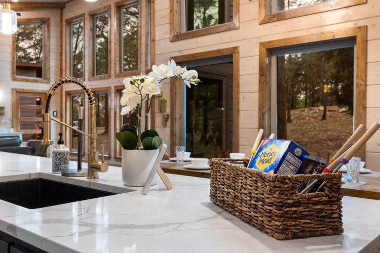 Kitchen sink and counter in front of tall windows, with a basket of cereal boxes