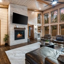Gas fireplace with a TV above it and leather chairs beneath tall windows