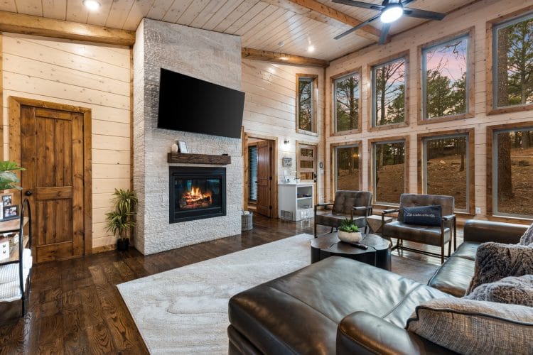 Gas fireplace with a TV above it and leather chairs beneath tall windows