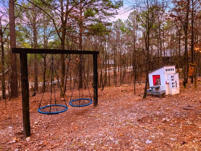 Two nest swings and a small white playhouse in the yard