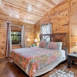 Bedroom with a bed under a paisley quilt, an X-pattern wood headboard, lamps on both sides and a window