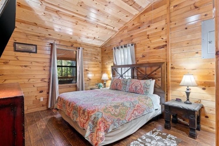Bedroom with a bed under a paisley quilt, an X-pattern wood headboard, lamps on both sides and a window