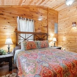 Closer view of the bed with a paisley quilt, wood headboard and a bedside lamp