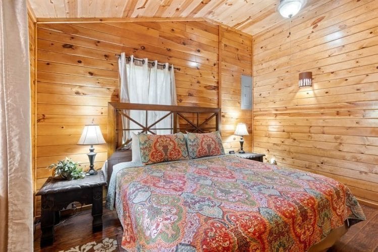 Closer view of the bed with a paisley quilt, wood headboard and a bedside lamp