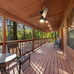 Covered porch with a ceiling fan, a round patio table and chairs, and a wood railing