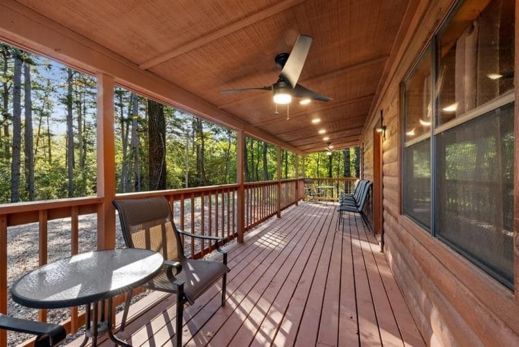 Covered porch with a ceiling fan, a round patio table and chairs, and a wood railing