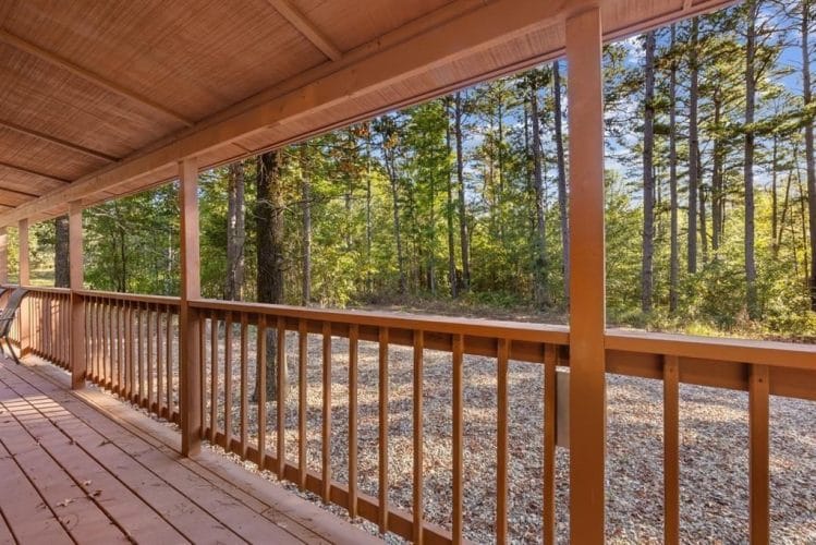 View along the covered porch railing out to the pine trees and gravel yard