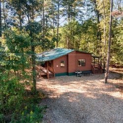 Side of the cabin with a green roof, gravel drive and trees