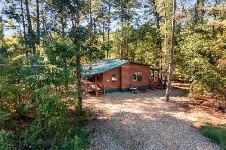 Side of the cabin with a green roof, gravel drive and trees