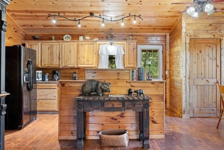 Kitchen with light wood cabinets, a black refrigerator and a dark wood console table, with the back door beside it
