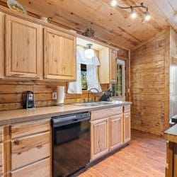 Kitchen counter with a coffee maker, a sink under a window and a black dishwasher
