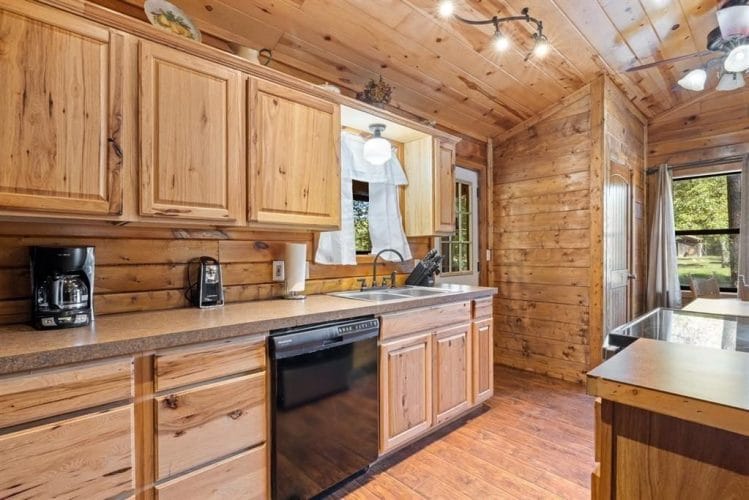 Kitchen counter with a coffee maker, a sink under a window and a black dishwasher