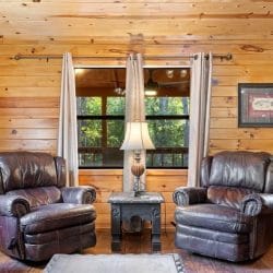 Two leather recliners with a lamp and side tables under a window, with a framed picture on the pine wall
