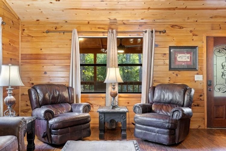 Two leather recliners with a lamp and side tables under a window, with a framed picture on the pine wall