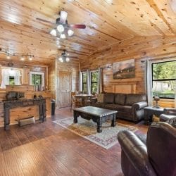 Open living area and kitchen under a pine ceiling with two ceiling fans, a leather sofa and recliners