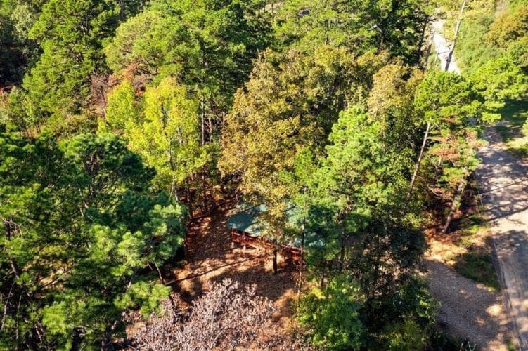 Aerial view looking down through trees at the cabin roof and gravel driveway