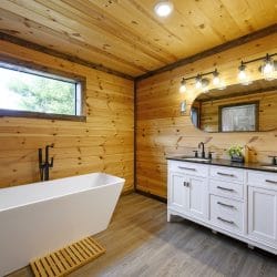 Bathroom with a freestanding tub, a double white vanity and pine walls
