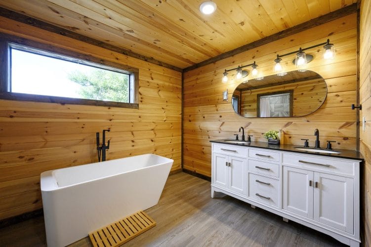 Bathroom with a freestanding tub, a double white vanity and pine walls