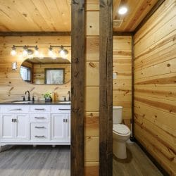 Double white vanity beside a wood post, with the toilet room at right