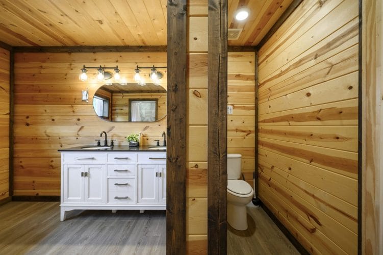 Double white vanity beside a wood post, with the toilet room at right