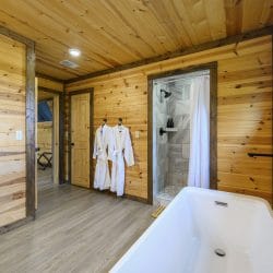 Freestanding tub with a black floor-mounted faucet, a walk-in shower beyond and two robes hanging