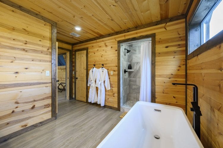 Freestanding tub with a black floor-mounted faucet, a walk-in shower beyond and two robes hanging