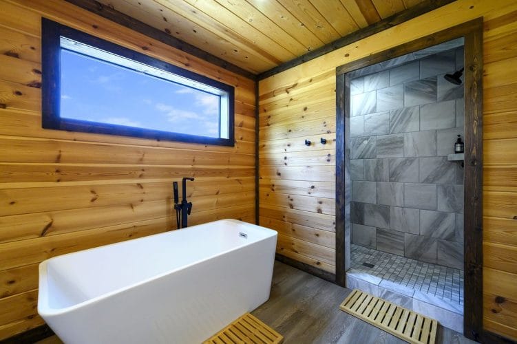Freestanding tub under a long window, with a tiled shower beside it