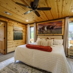 King bed with white quilted bedding under a pine ceiling, a longhorn print and an open bathroom door