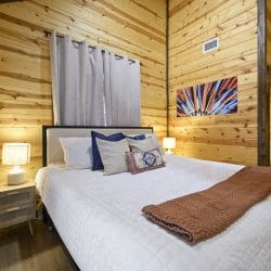 Bed with a white quilt, navy pillows and a brown throw beside a curtained window
