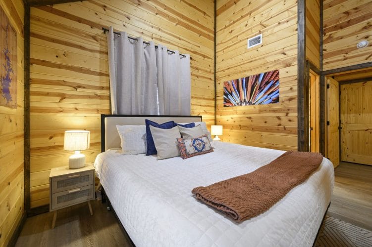 Bed with a white quilt, navy pillows and a brown throw beside a curtained window