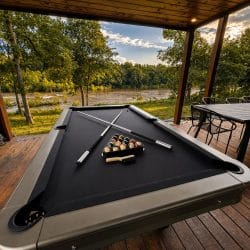 Outdoor pool table on the covered porch with a river and field view beyond