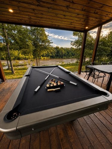 Outdoor pool table on the covered porch with a river and field view beyond