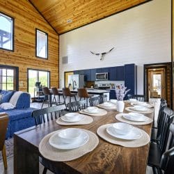 Dining table set with plates and black chairs, the sectional and kitchen behind