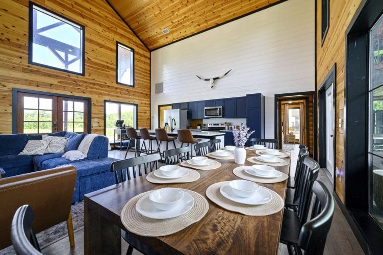 Dining table set with plates and black chairs, the sectional and kitchen behind