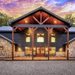 Front of the stone-and-dark-siding cabin with a timber gable porch lit at dusk