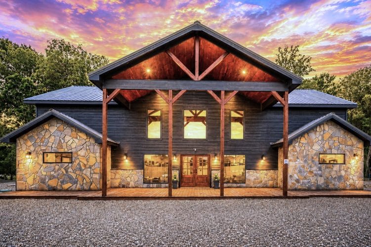 Front of the stone-and-dark-siding cabin with a timber gable porch lit at dusk