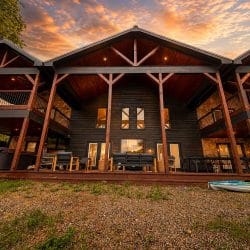Rear of the cabin with timber columns, upstairs balconies and kayaks on the grass at sunset