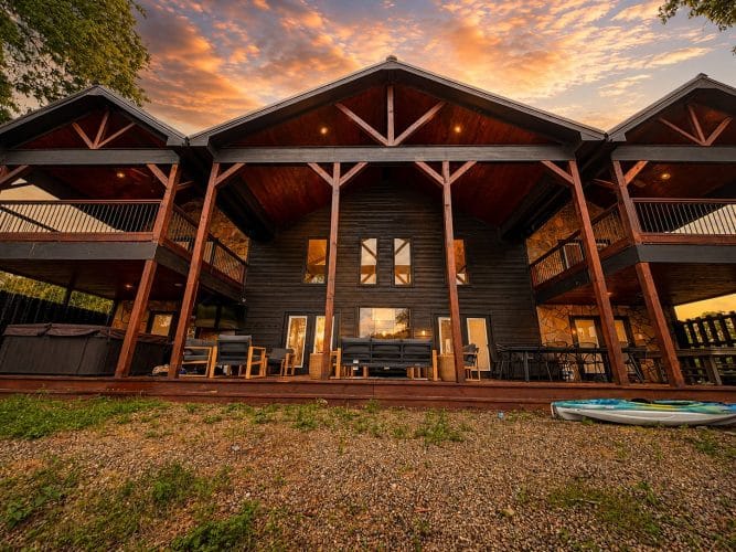 Rear of the cabin with timber columns, upstairs balconies and kayaks on the grass at sunset