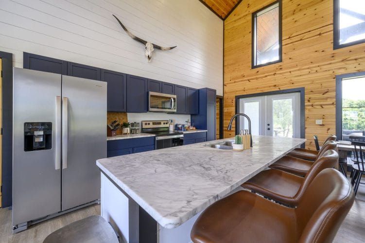 Kitchen with a stainless refrigerator, navy cabinets and an island with leather stools