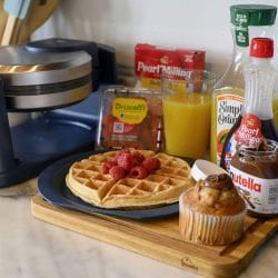 Waffle with berries, orange juice, syrup and a muffin on a tray beside a waffle maker