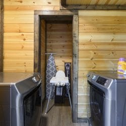 Side-by-side washer and dryer with an ironing board and a high chair in the laundry room