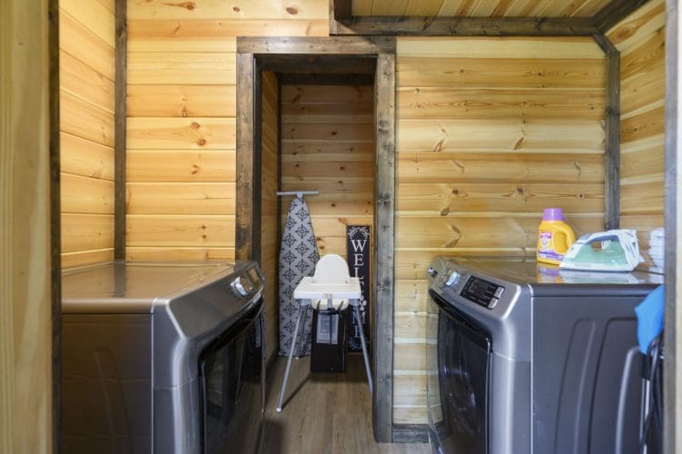 Side-by-side washer and dryer with an ironing board and a high chair in the laundry room