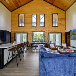 Great room with blue sofas, a counter with leather stools and a tall pine wall with narrow windows