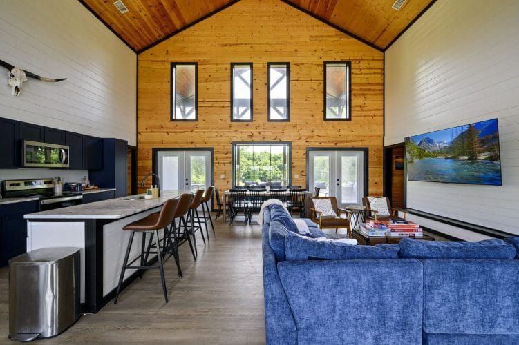 Great room with blue sofas, a counter with leather stools and a tall pine wall with narrow windows