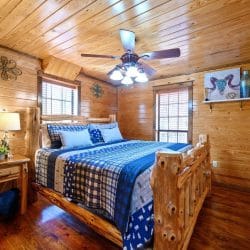 Bedroom with a king-size log-post bed, a blue plaid and bear-print quilt, a nightstand and a ceiling fan