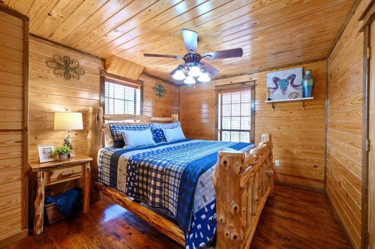 Bedroom with a king-size log-post bed, a blue plaid and bear-print quilt, a nightstand and a ceiling fan