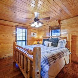 Second bedroom with a log-post bed, gray plaid comforter and a ceiling fan